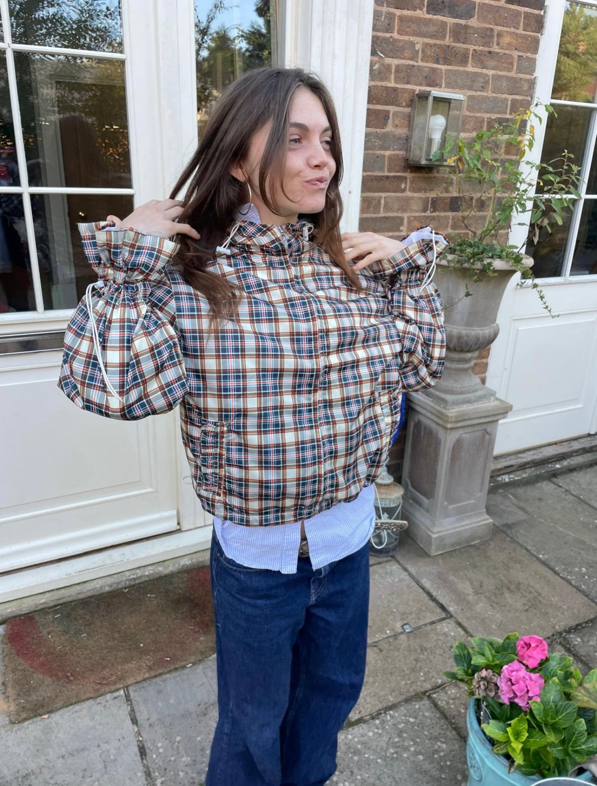 Person wearing a plaid shirt outdoors with a house and garden in the background