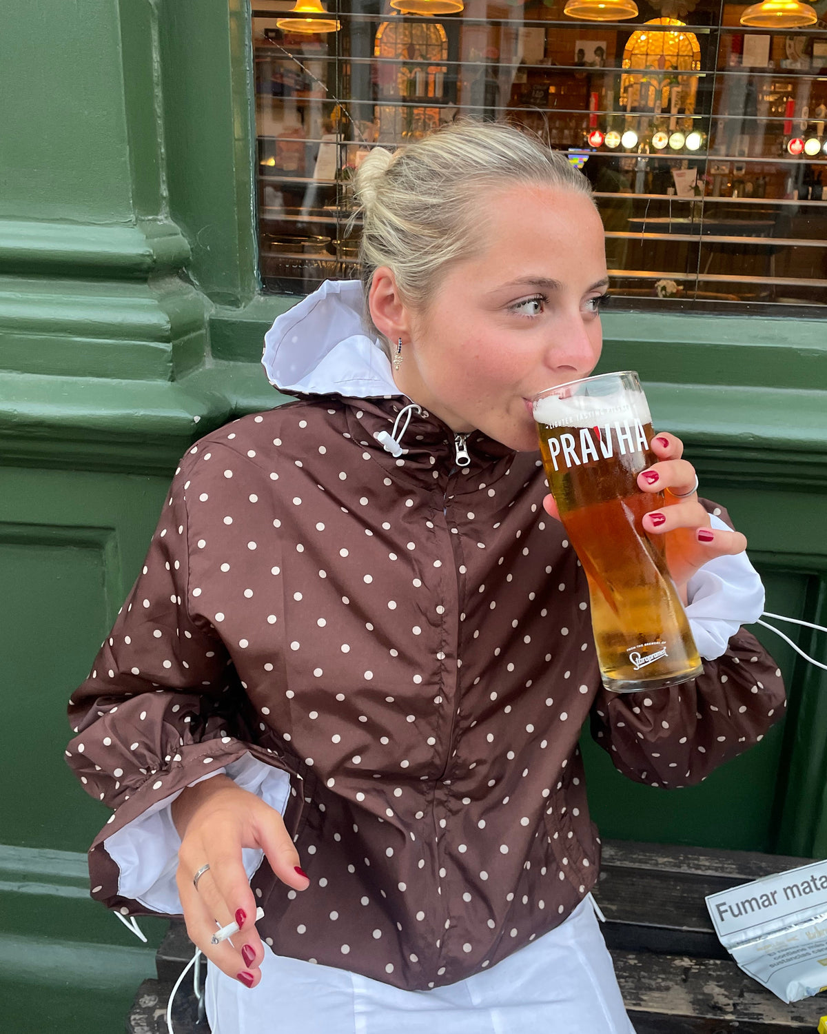 Person in a brown polka dot jacket drinking from a glass bottle with a blurred background