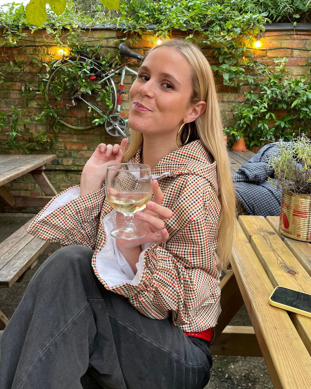 a woman in a pub drinking wine with a male gingham flared windbreaker on