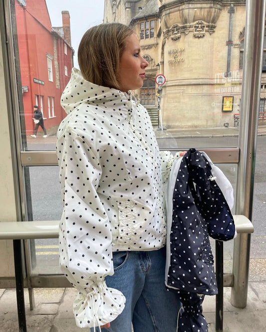 Person wearing a white raincoat with black polka dots at a bus stop.