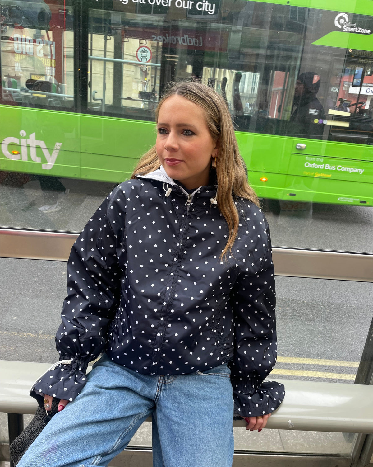 A person wearing a navy and cream polka dot waterproof windbreaker with a white collar, paired with blue jeans.
