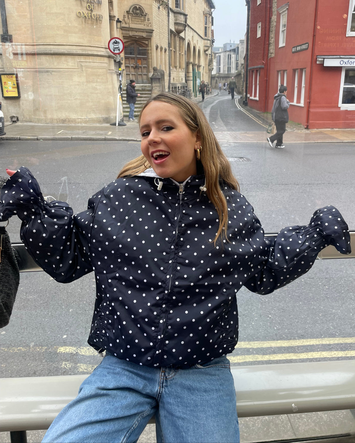 A woman wearing a polka dot flared windbreaker with blue jeans 