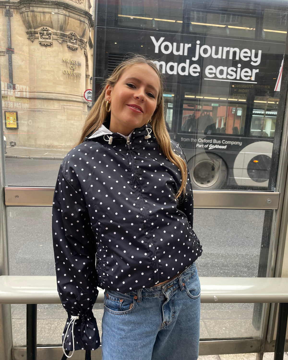 A woman wearing a polka dot flared windbreaker with blue jeans