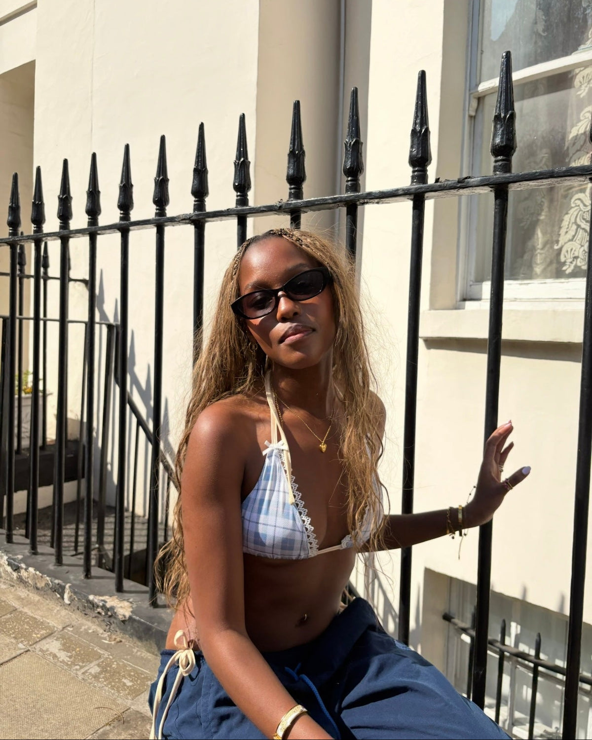 Woman sitting on a black metal fence wearing sunglasses and a blue and white outfit.