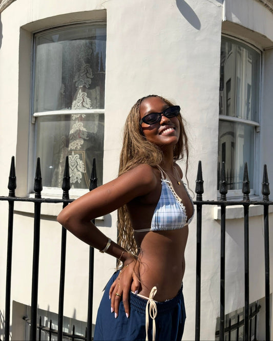 Woman in a bikini top and sunglasses standing in front of a white building with black railings.
