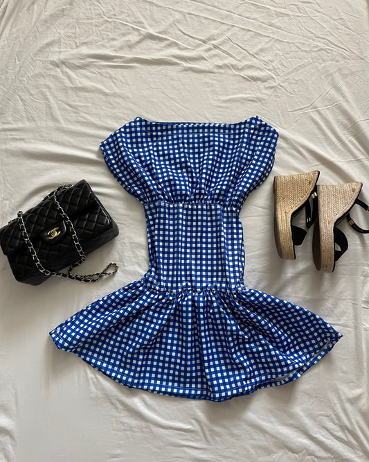 Blue checkered bow skirt with black wedge sandals and a black handbag on a white surface