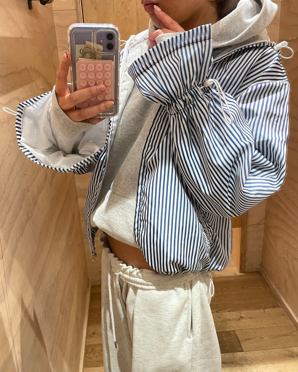 Person wearing a striped windbreaker and holding a phone on a wooden floor.