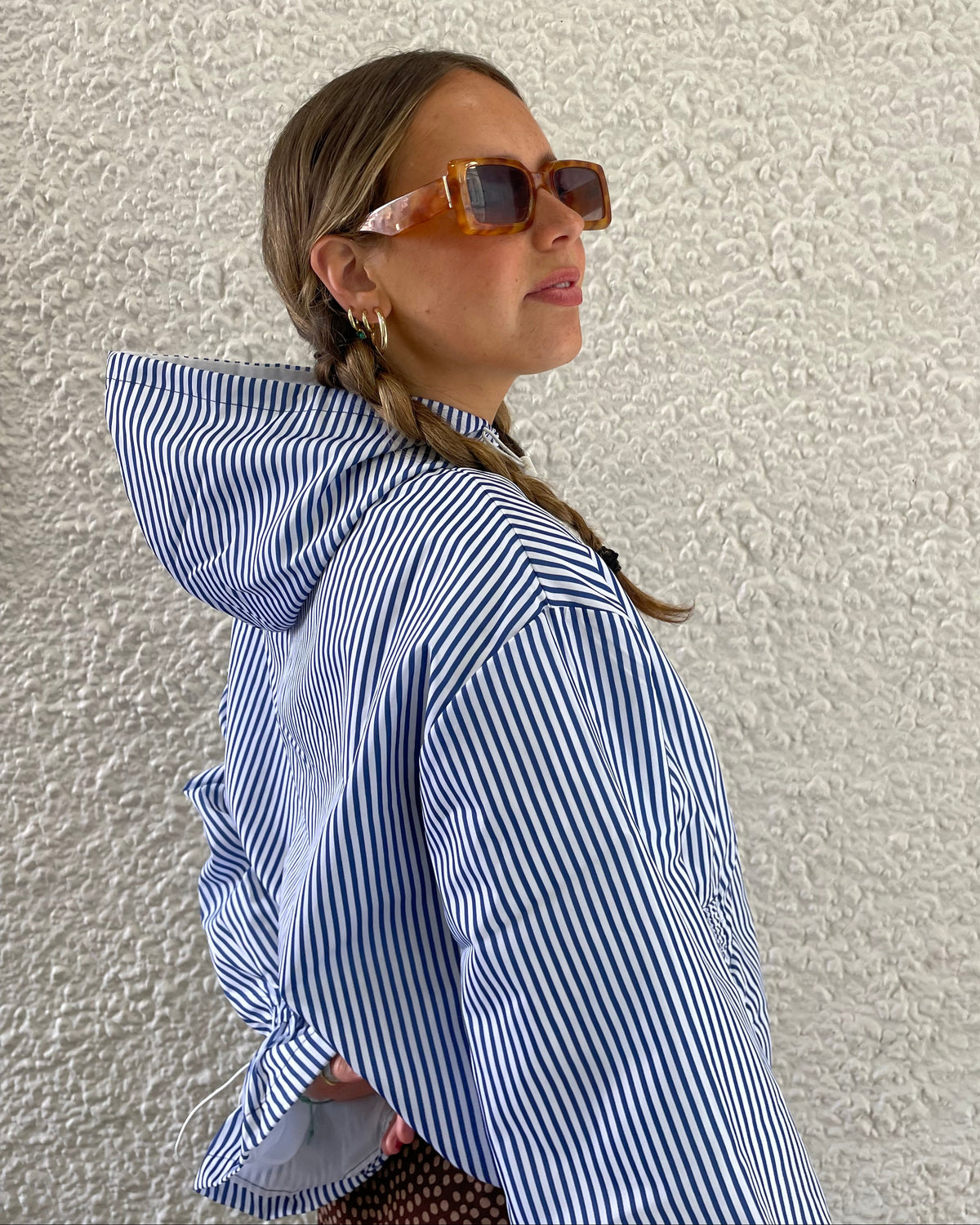 Woman wearing a blue and white striped windbreaker against a textured beige wall.