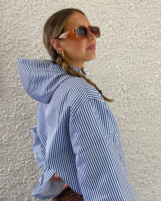 Woman wearing a blue and white striped windbreaker against a textured beige wall.