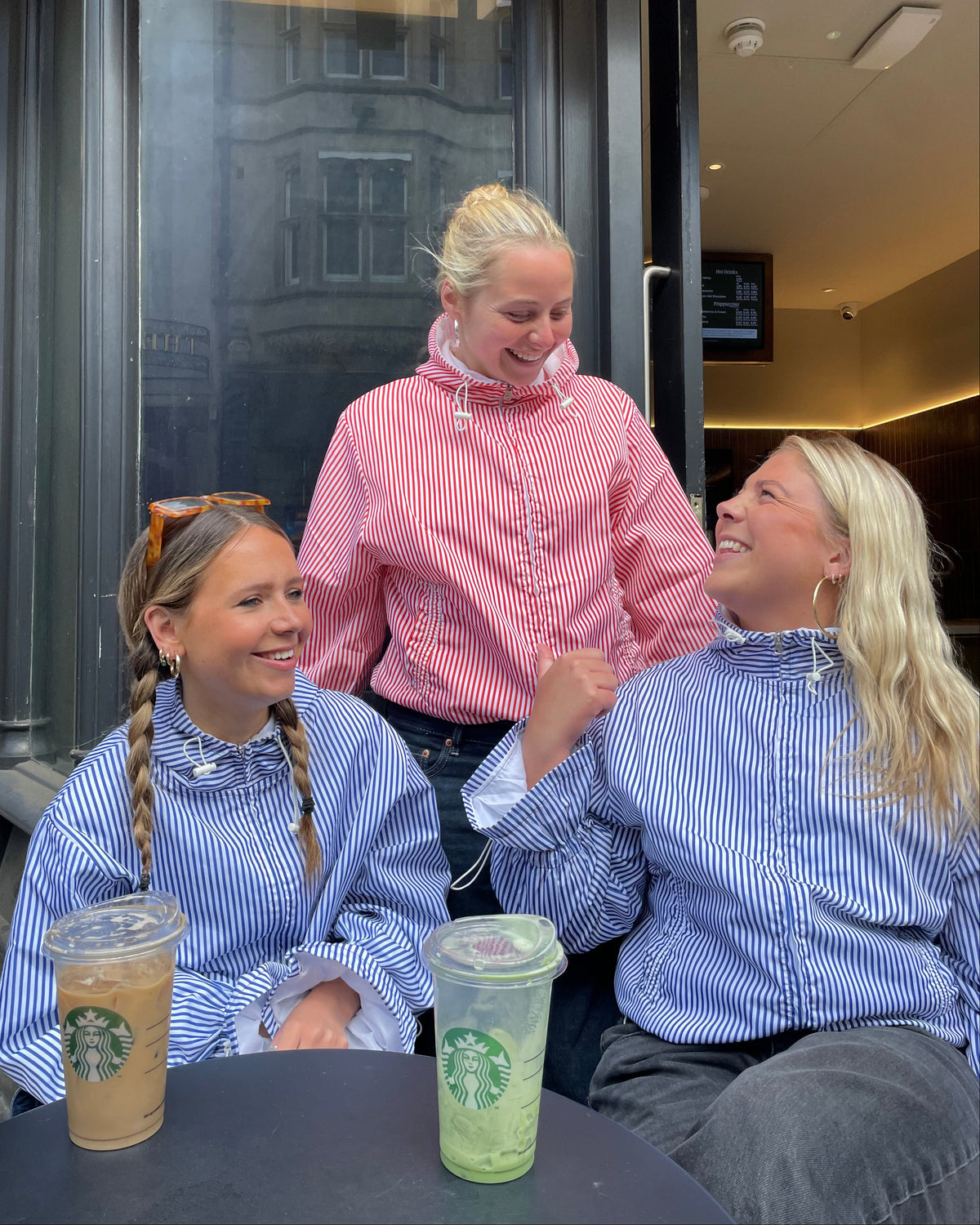 Two women in matching striped outfits sitting at a table with Starbucks drinks.