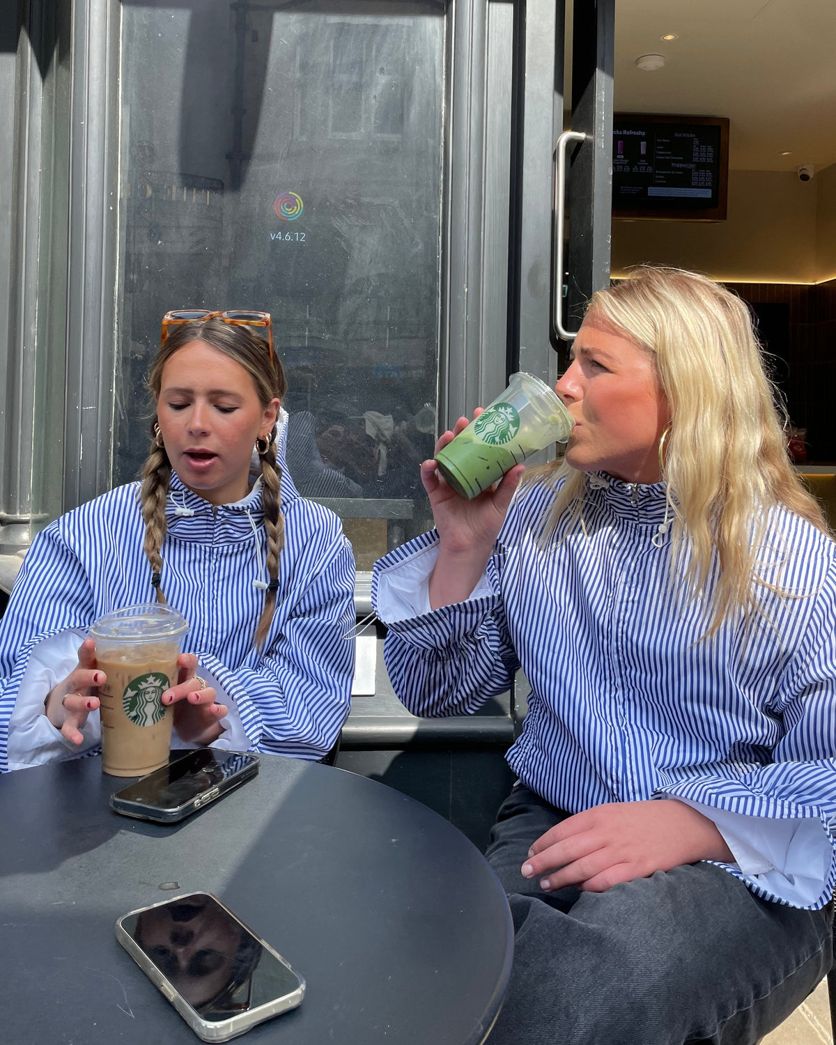 Two people in matching blue and white striped shirts holding Starbucks drinks in front of a glass door.