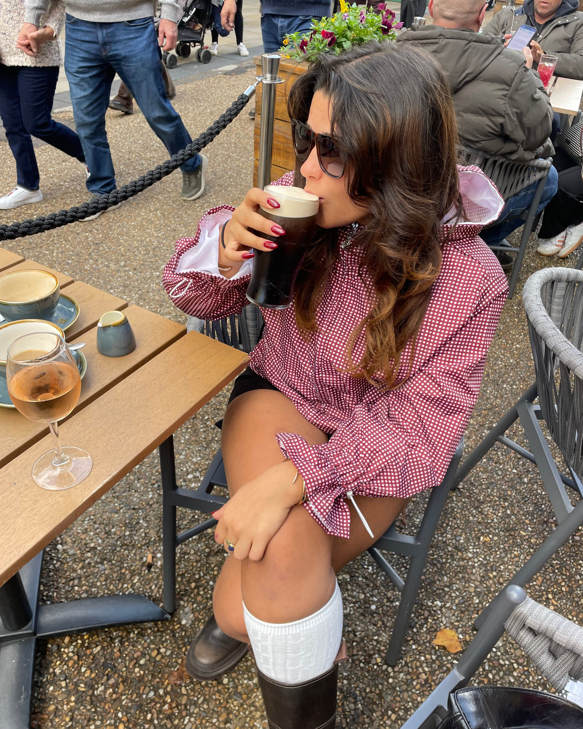 Woman sitting at a table outdoors, drinking from a cup.