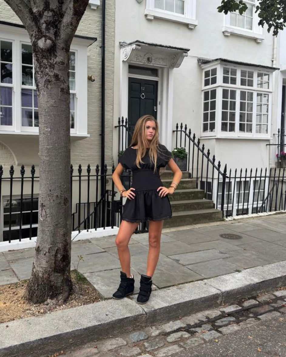 Woman in a black dress standing on a street with a white building in the background