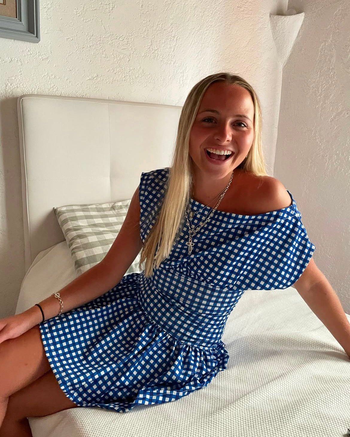 Woman in a blue and white checkered dress sitting on a bed.