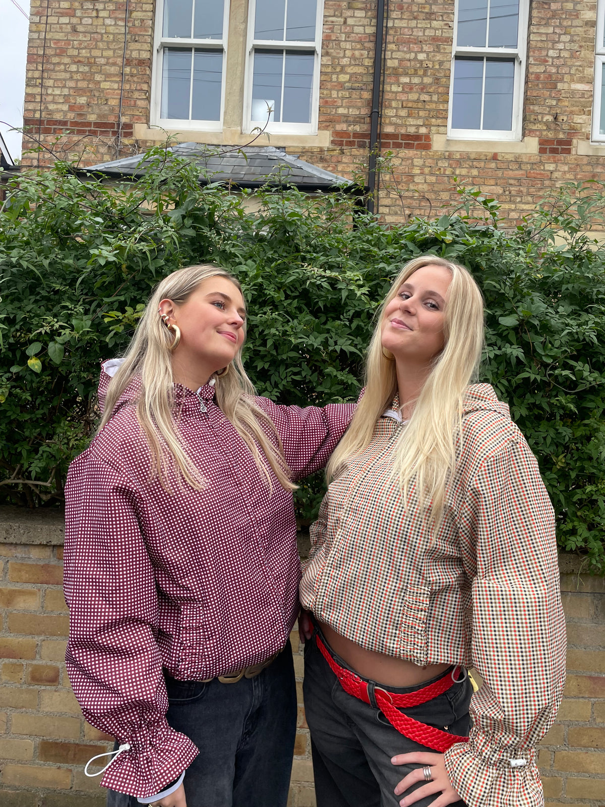 2 women against a wall wearing gingham windbreakers in cherry and maple with flared sleeves