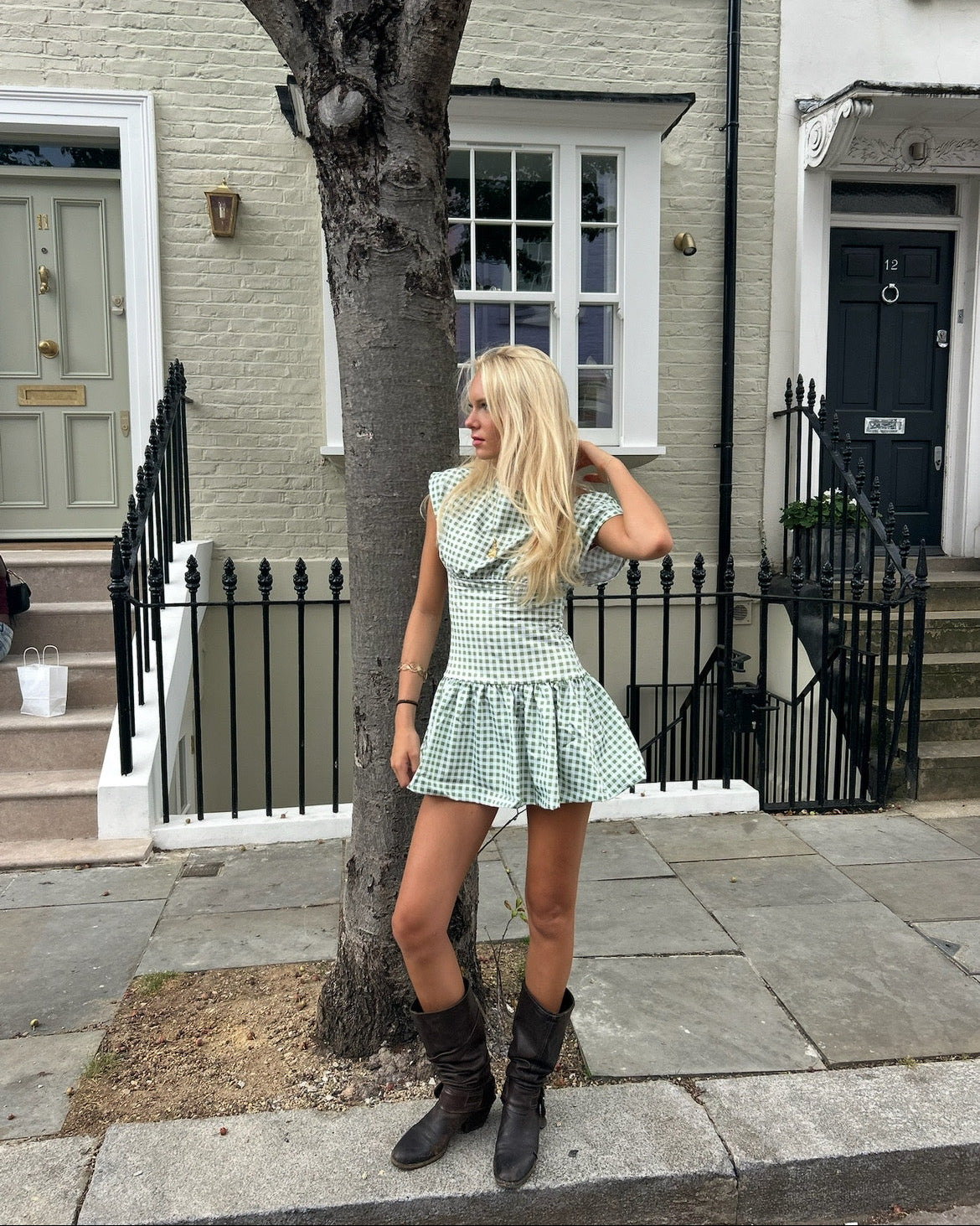 Woman in a checkered dress standing next to a tree on a street.