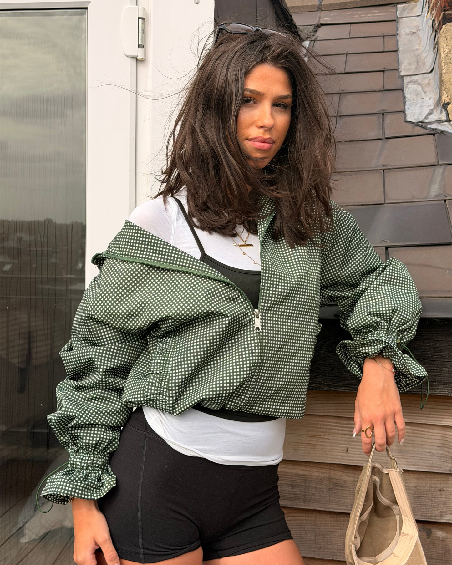 A woman wearing a olive gingham windbreaker jacket styled with layered tops and shorts 