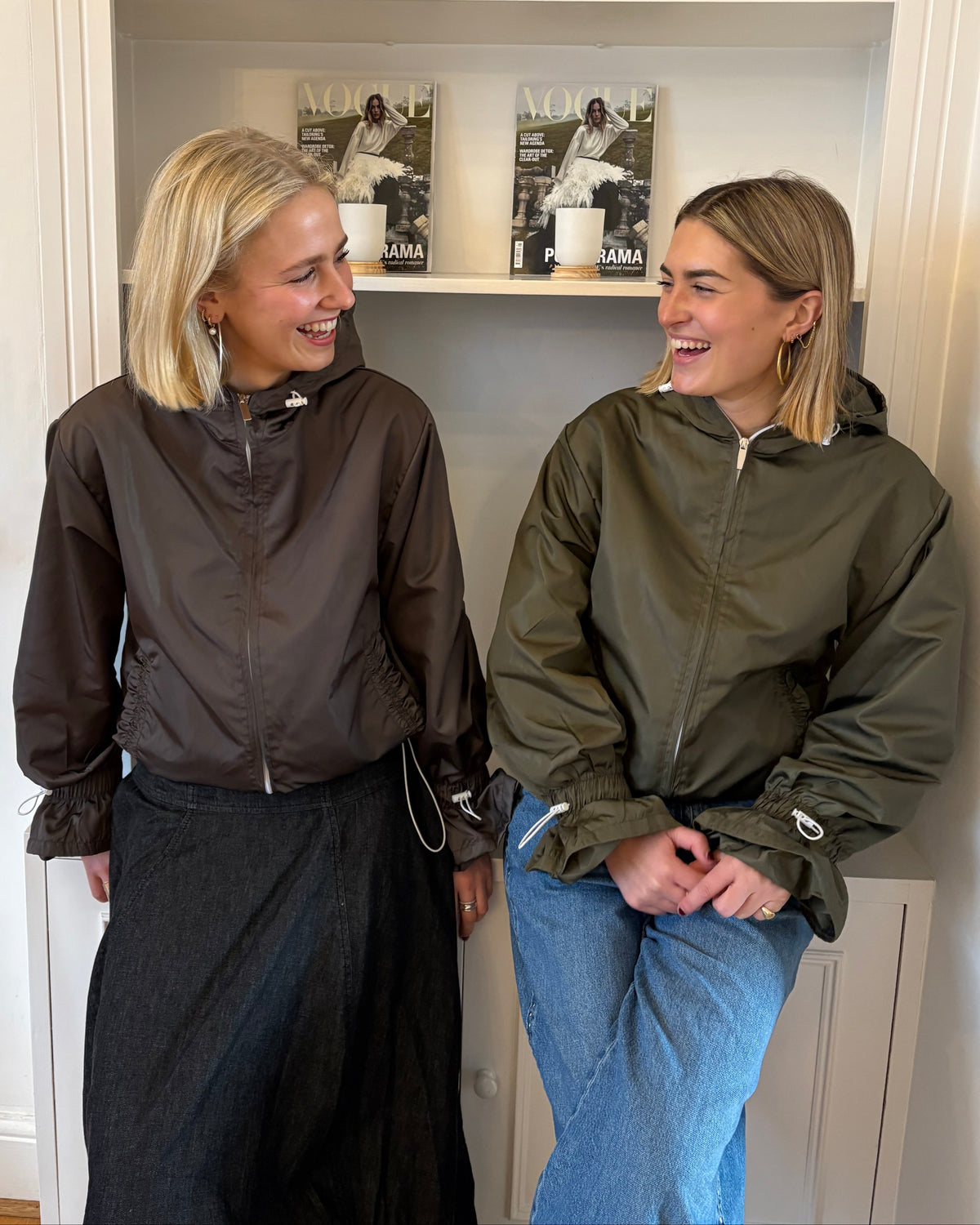 Two women standing in front of a mirror trying on jackets.