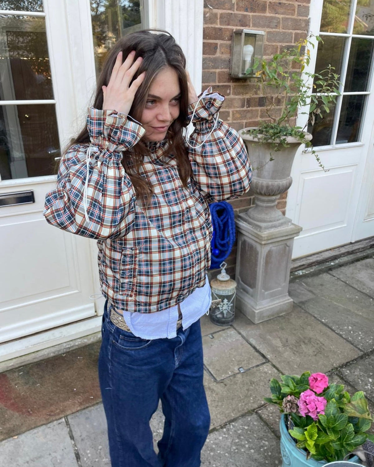 Person wearing a plaid shirt and blue jeans standing outside a house.