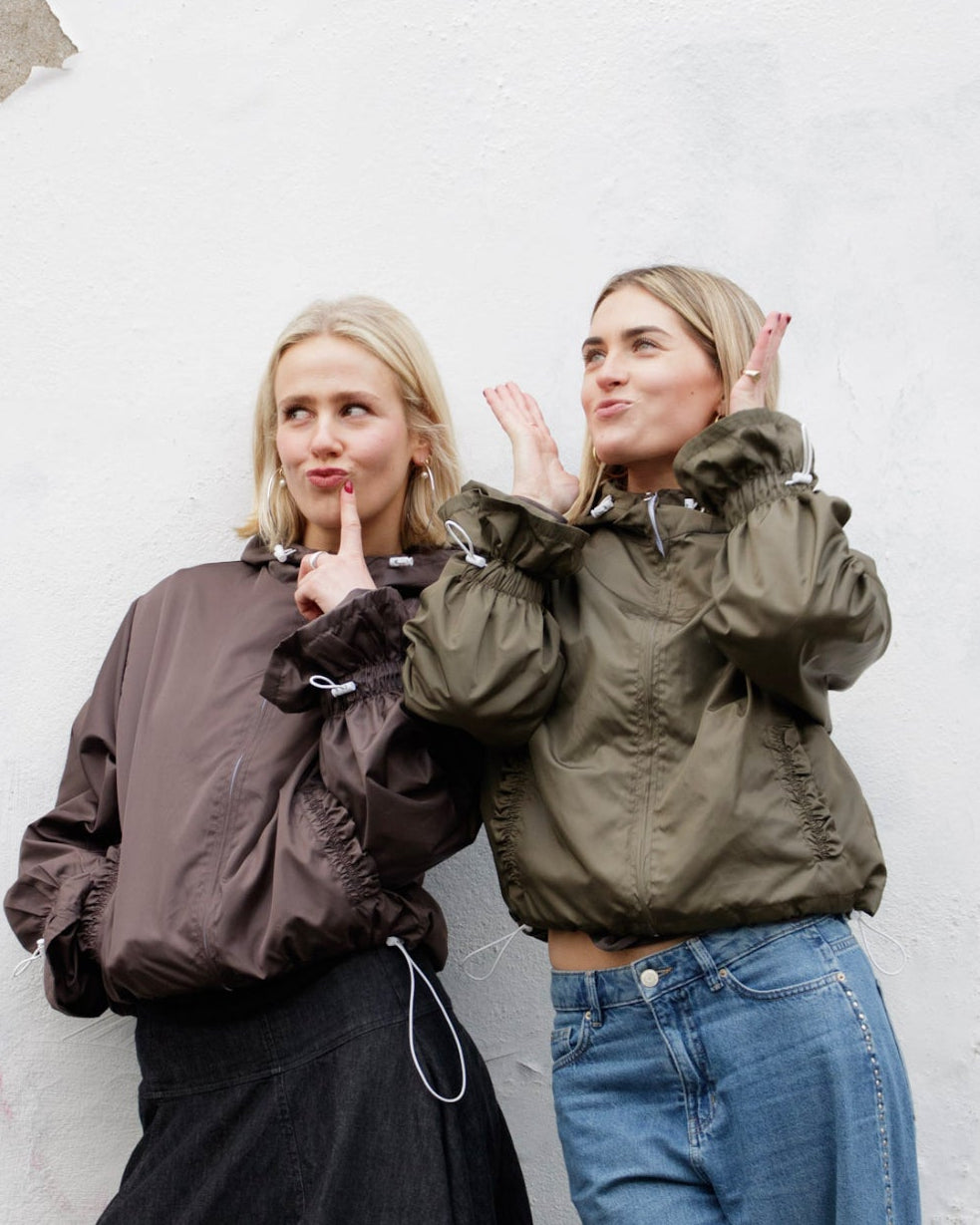 Two women posing against a textured white wall.