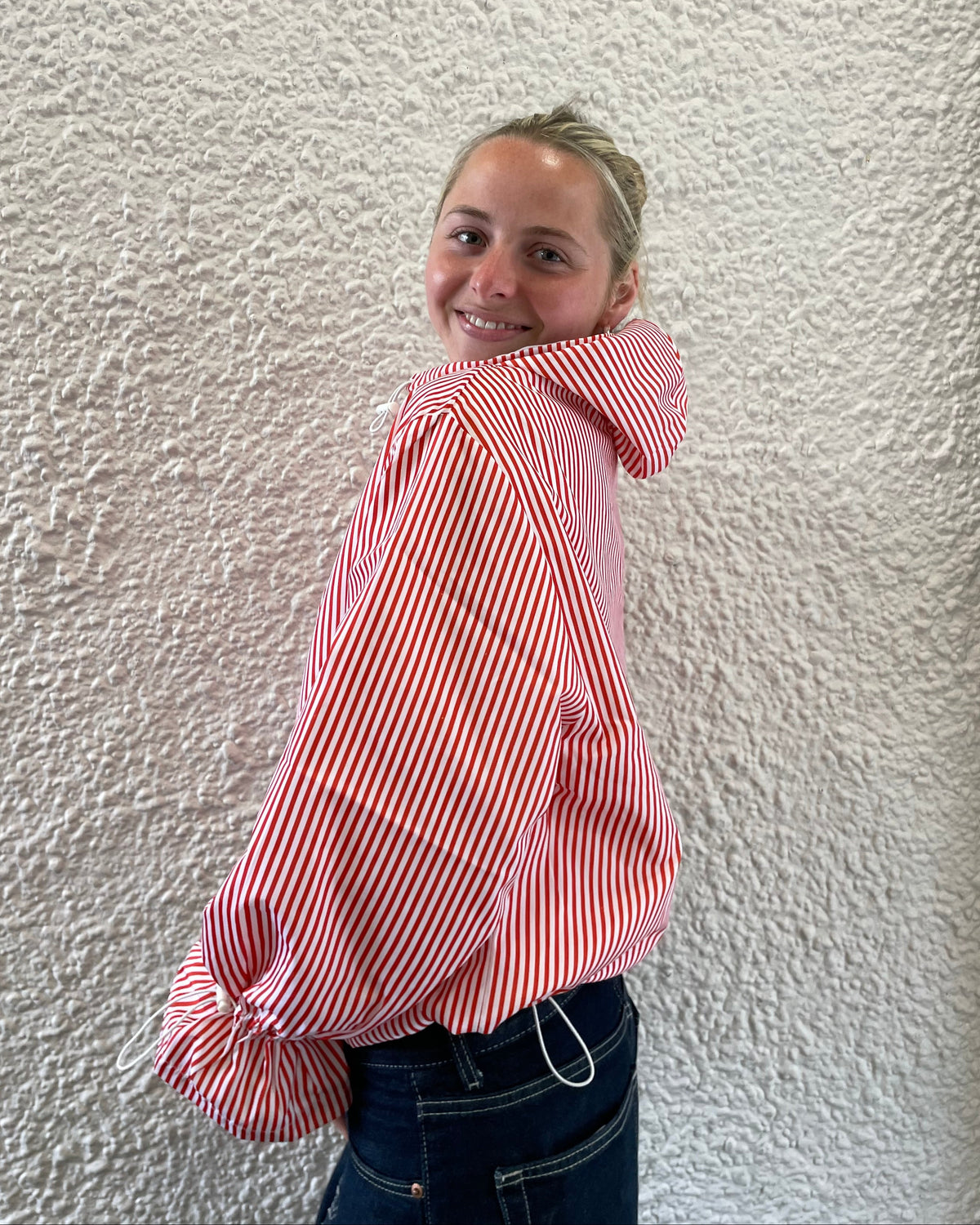 Person wearing a red and white striped shirt on a textured white wall