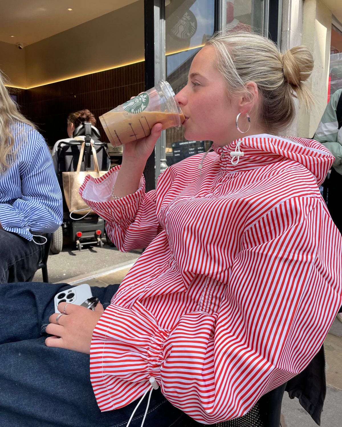 Person in a red and white striped shirt eating a sandwich outdoors.