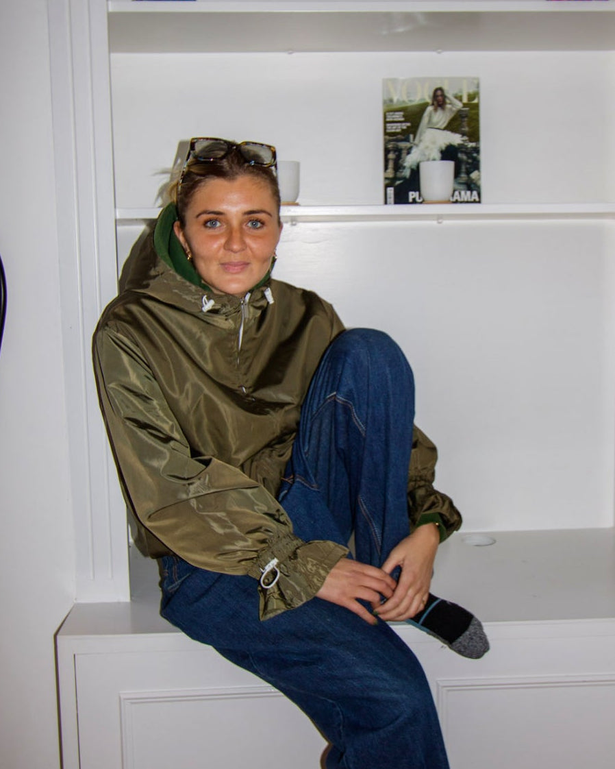 Person sitting on a white bench in front of a bookshelf with decorative items.