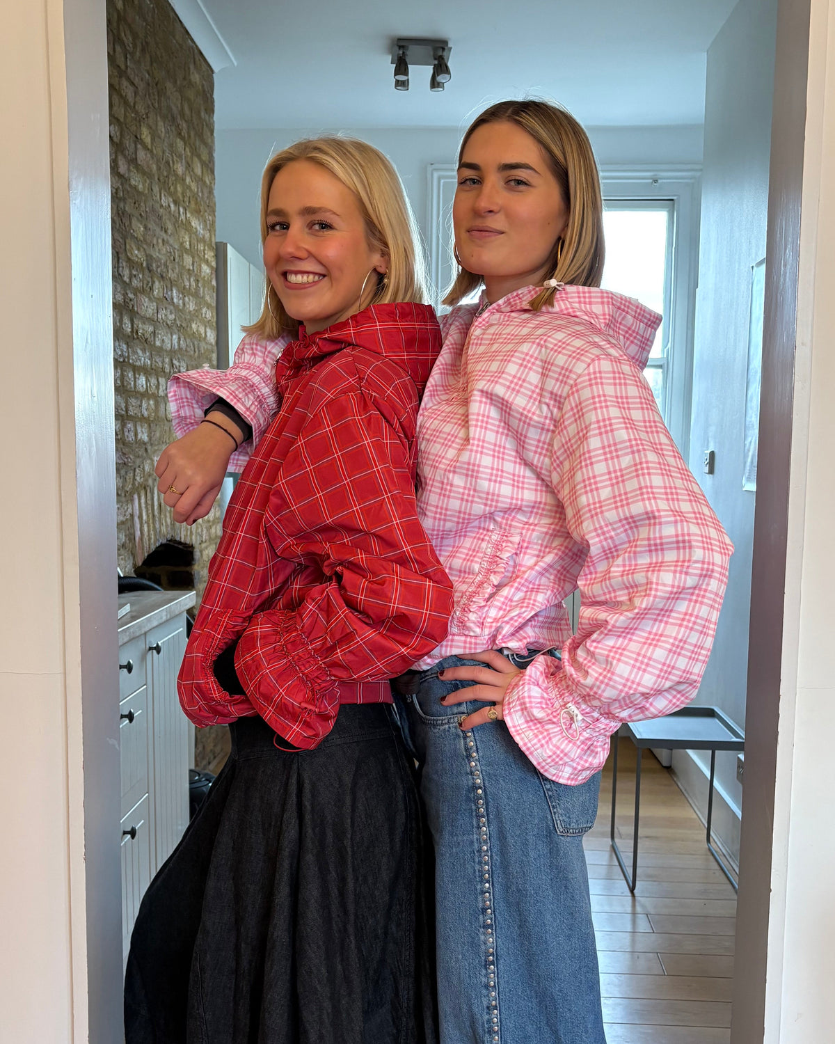 Two people standing inside a small room with a mirror reflecting their image.