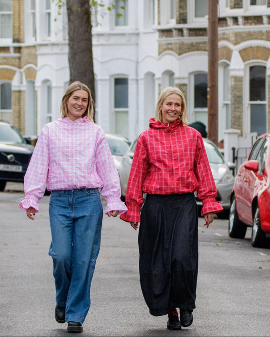 Two women walking down a street holding hands, wearing colorful raincoats.